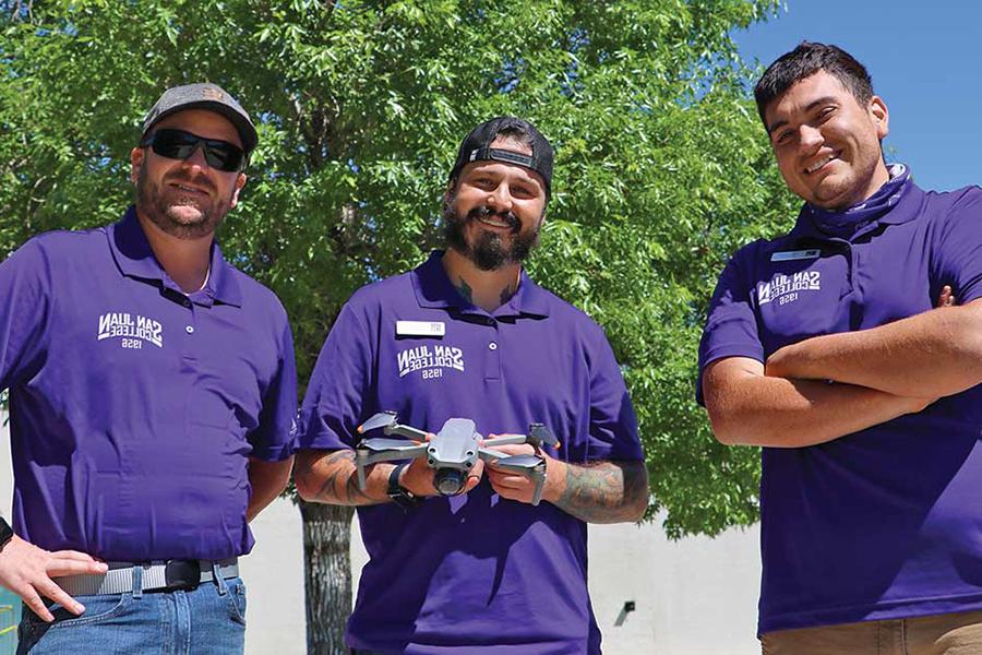 三个穿着紫色衬衫的人站在那里，手里拿着一架无人机